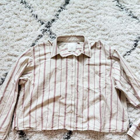 UNIQLO x JW Anderson Striped Long Sleeve Button-Up Shirt in an off-white/cream base with burgundy and tan ticking stripes. Measurements in photos!

Features a cropped, boxy silhouette by design, structured point collar, single front chest pocket, embroidered "JWA" tonal logo on the lower left hem, and a modern relaxed fit. A clean, stylish piece from the popular designer collaboration.

 Brand: Uniqlo x JW Anderson
 Size: Men’s Large (Pit-to-pit: ~23.5", Length: ~20" cropped fit by design)
 Colorway: Off-White / Burgundy Striped
 Condition: Excellent pre-owned condition; fabric is crisp with no stains, discoloration, or missing buttons. Embroidered logo detail is sharp.

#jwanderson #fallstyle #cropped #stripedshirt #streetwear